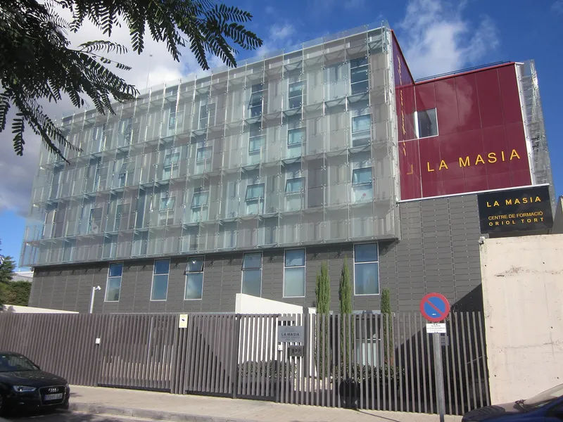 Gedung La Masia Centre de Formació Oriol Tort berdinding kaca dengan papan nama merah