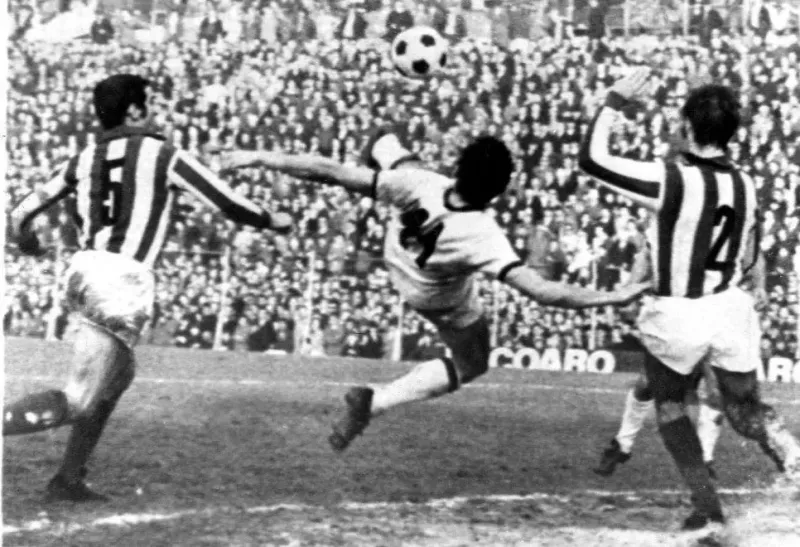 Foto hitam putih Gigi Riva melakukan rovesciata di udara di antara dua pemain Vicenza berseragam garis
