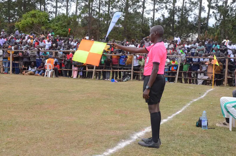 Asisten wasit berkaus merah muda membentangkan bendera kotak-kotak oranye kuning di pinggir lapangan