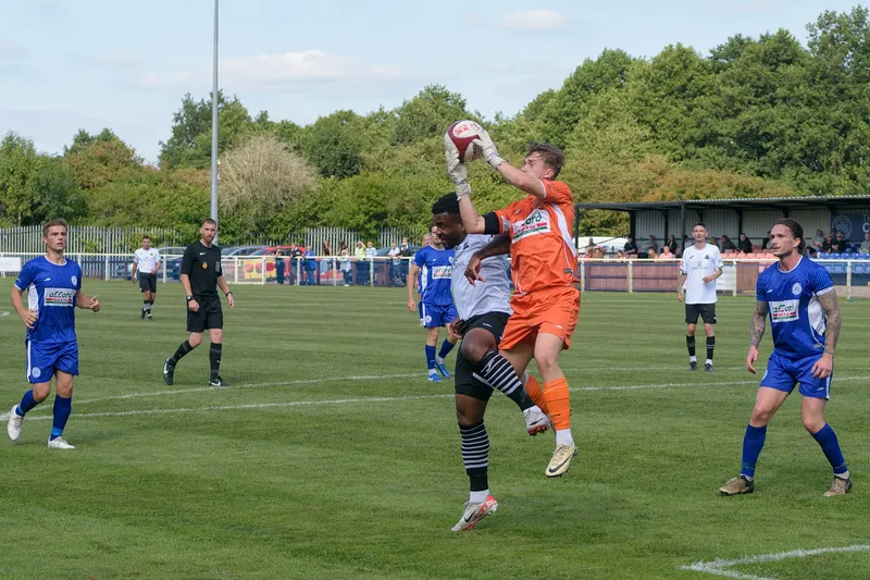 Kiper Hanley Town berseragam oranye melompat menangkap bola dengan kedua tangan di depan penyerang Lichfield City