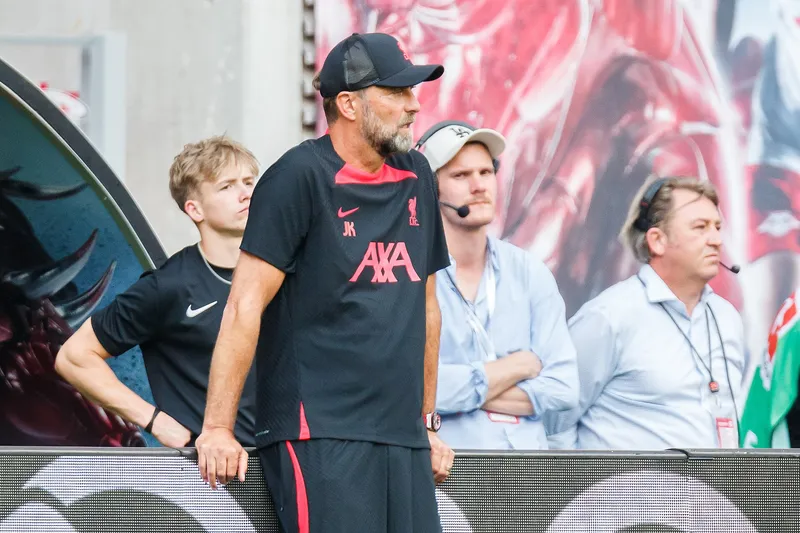 Jürgen Klopp bertopi dan berkaus latihan Liverpool berdiri di pinggir lapangan