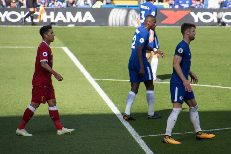Roberto Firmino berseragam merah Liverpool berjalan di dekat dua bek Chelsea berseragam biru