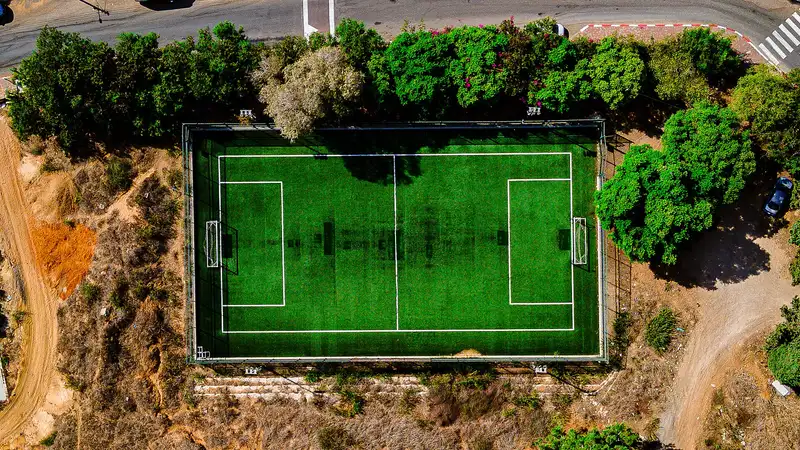Lapangan sepak bola rumput sintetis dilihat tegak lurus dari atas, lengkap dengan garis tengah dan dua kotak penalti