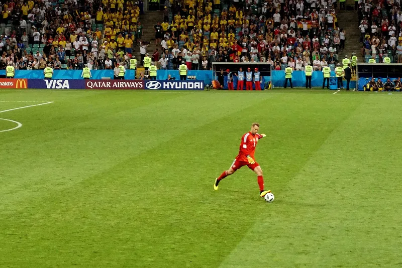 Kiper Jerman Manuel Neuer berkostum merah menendang bola di lapangan dengan tribun penuh suporter Swedia berbaju kuning