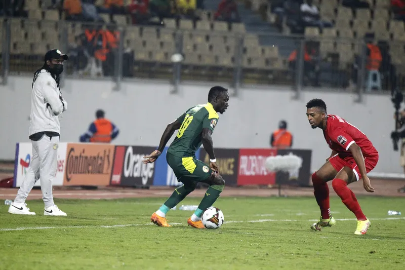 Sadio Mane berseragam hijau Senegal menggiring bola berhadapan satu lawan satu dengan bek berseragam merah di dekat garis tepi