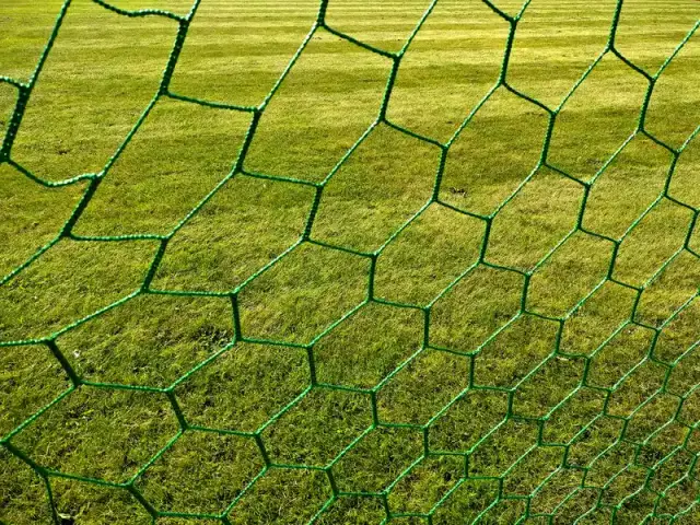 Jaring gawang sepakbola berwarna hijau bermata heksagonal dengan latar rumput lapangan