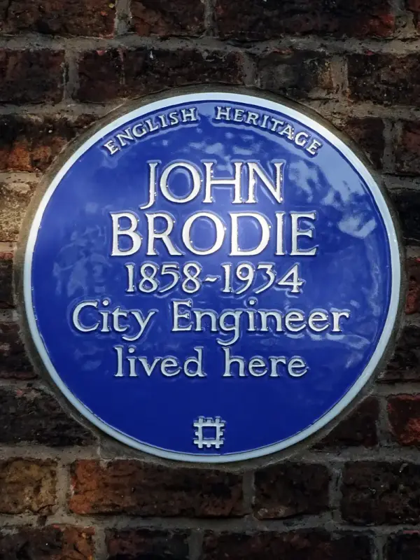Plakat biru English Heritage bertuliskan John Brodie 1858-1934 City Engineer lived here di dinding bata