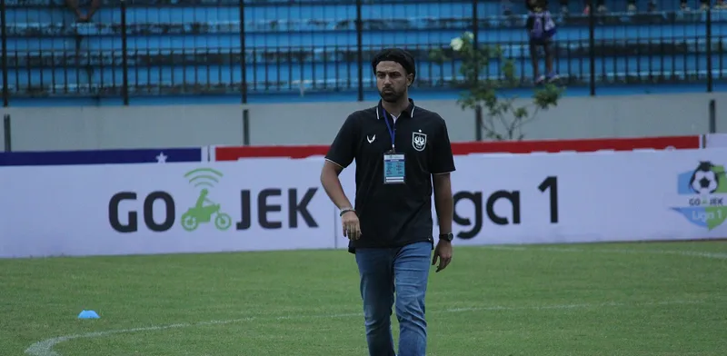 Pelatih PSIS Semarang berkaus hitam berjalan di pinggir lapangan di depan papan iklan Go-Jek Liga 1
