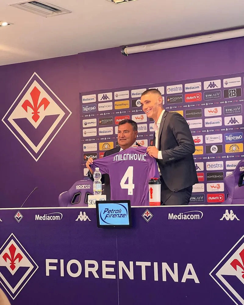 Nikola Milenkovic dan Joe Barone memegang jersey ungu Fiorentina bertuliskan Milenkovic nomor 4