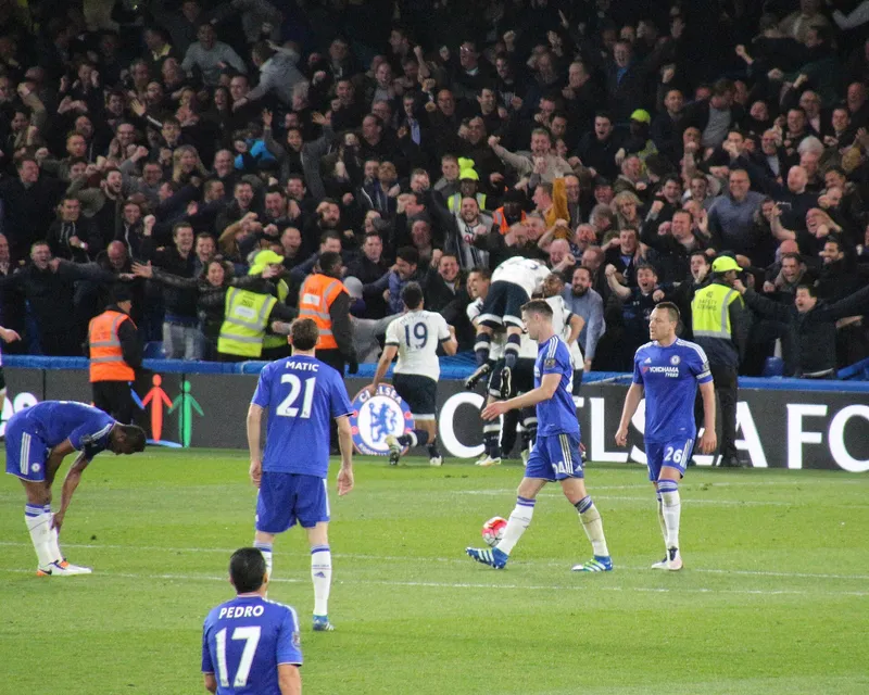 Pemain Tottenham berpelukan merayakan gol di depan tribun suporter sementara pemain Chelsea berbaju biru tertunduk