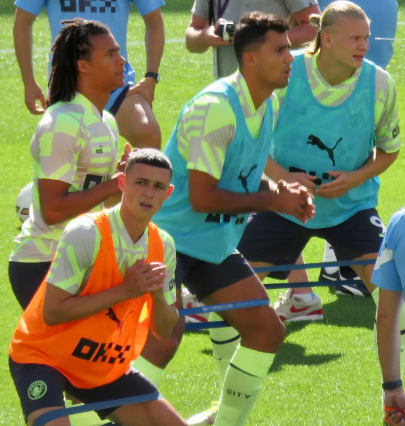 Pemain Manchester City berompi latihan melakukan gerakan jongkok dengan karet resistensi di kaki