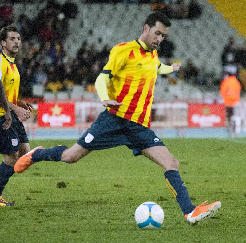 Sergio Busquets berseragam kuning bergaris merah Catalonia bersiap mengoper bola