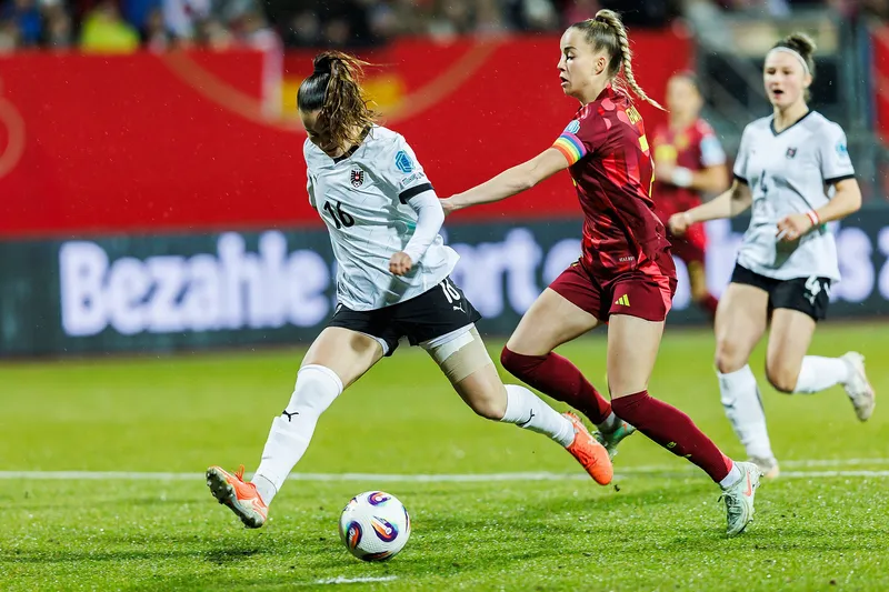 Pemain Jerman berbaju merah berlari mengejar pemain Austria berbaju putih yang bersiap menendang bola