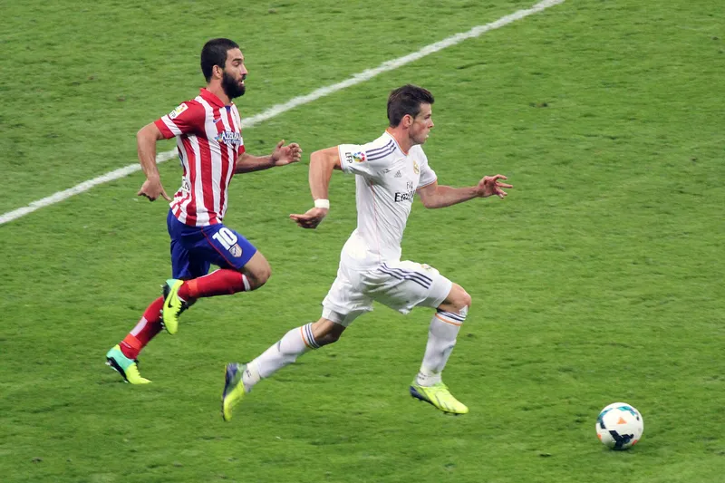 Gareth Bale berseragam putih Real Madrid berlari mengejar bola diikuti Arda Turan berseragam Atletico Madrid