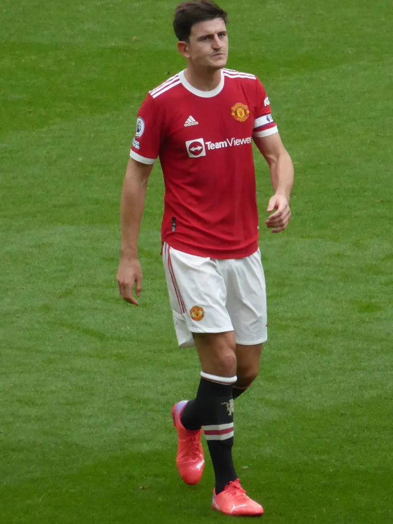 Harry Maguire berseragam merah Manchester United dengan ban kapten berjalan di lapangan