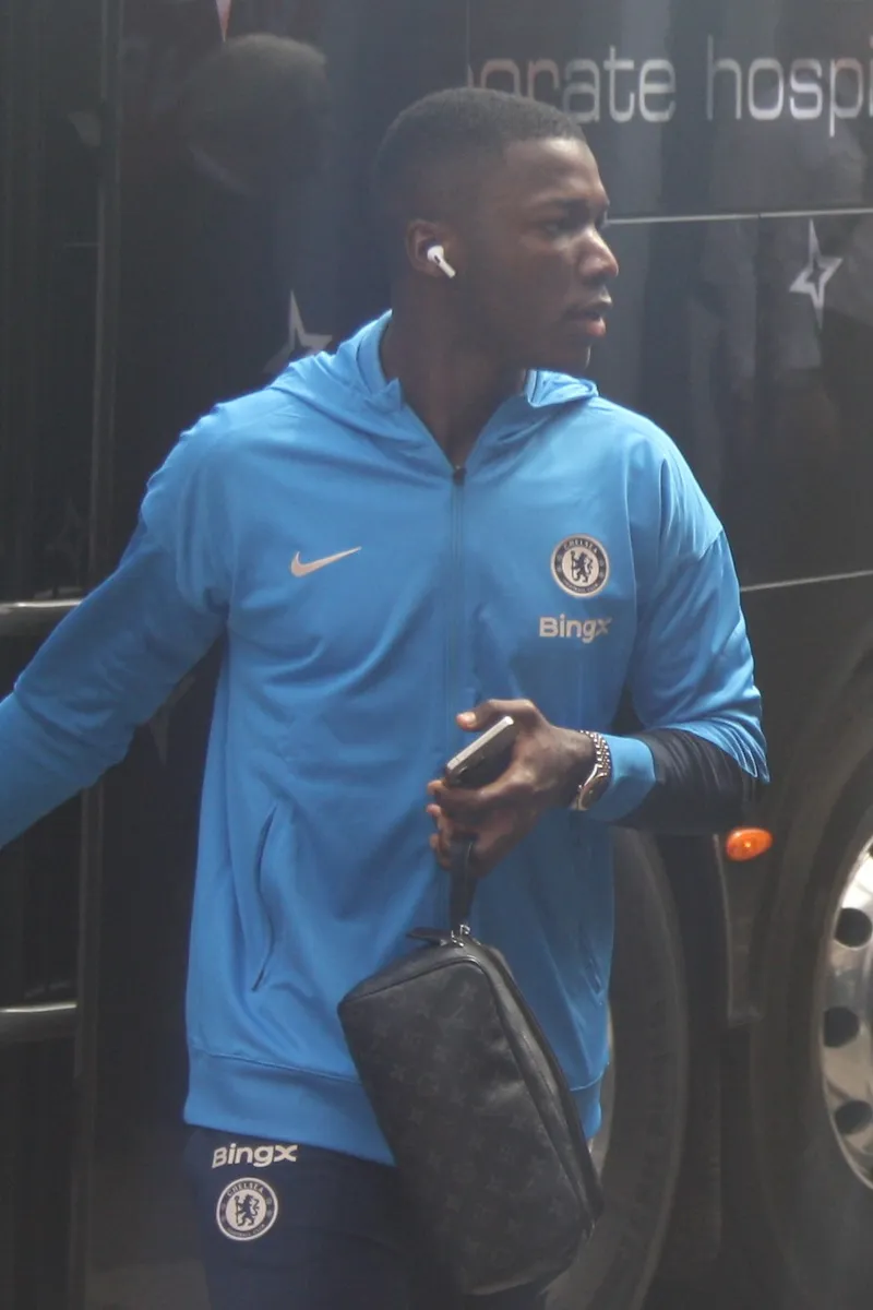 Moises Caicedo berjaket biru Chelsea turun dari bus tim sambil membawa tas