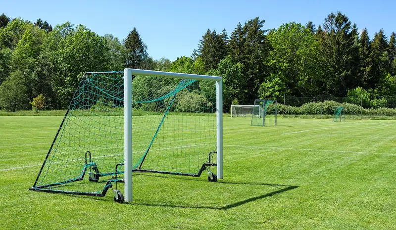 Gawang portabel berjaring hijau dengan roda dan rangka pemberat di lapangan latihan berumput