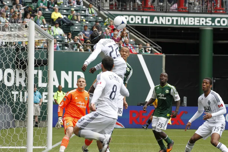 Darren Mattocks berseragam putih melompat menyundul bola di depan gawang Portland Timbers dengan kiper berseragam oranye